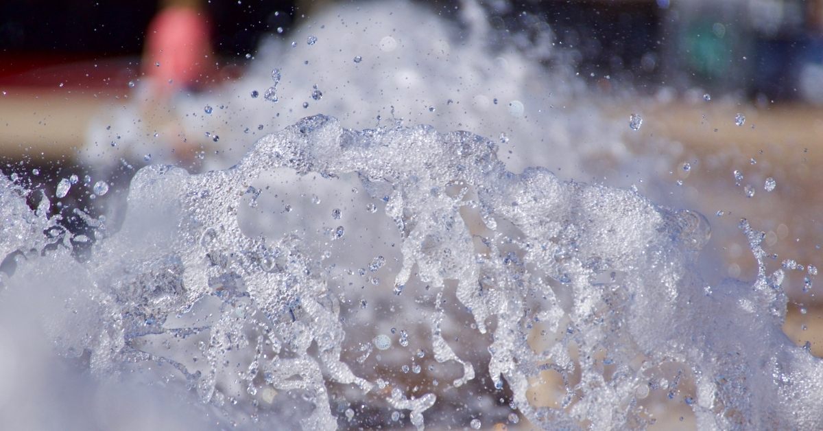 A close-up of water splashing energetically, with clear droplets and a blurred background featuring warm and cool tones.